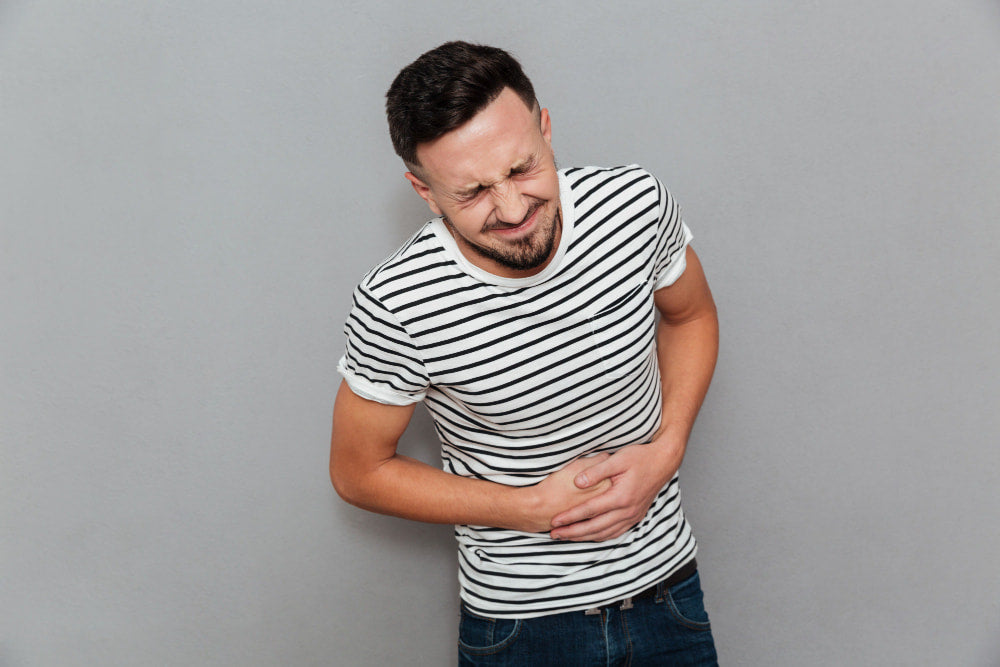 Hombre tocándose el abdomen con expresión de sufrir un dolor abdominal agudo o cólico severo.